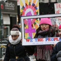 WE THE PEOPLE sign framing woman in pussy hat