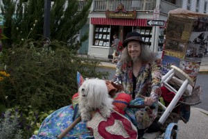 bearded man, long skirt, guiding the extravagantly decorated tricycle of bearded woman