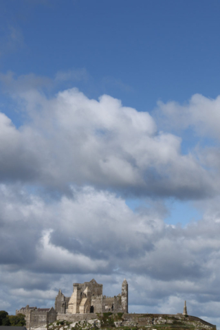 massive hillside castle ruins, deep blue sky, fluffs of dramatic clouds