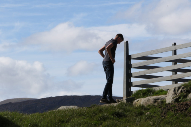 solitary figure, a young sheep farmer, head bent, silhouetted at top of hill