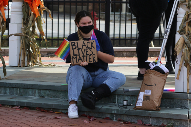 seated woman with black lives matter and gay rights signs