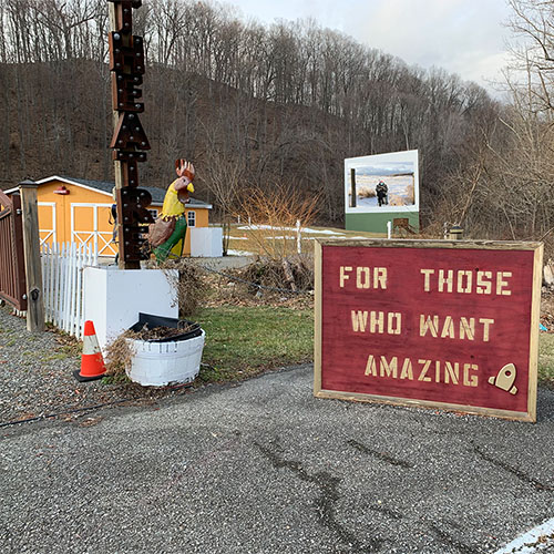 red sign on blacktop white lettering For Those Who Want Amazing Drive in theater screen in background