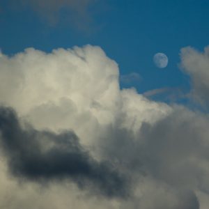 white clouds, black streaks full moon in blue sky