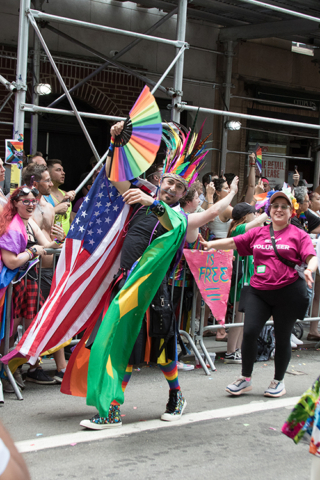 Man in feather headress with American flag and large fan in pride colors