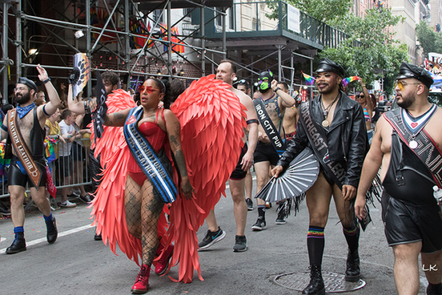 Ms Leather n red bustier and boots and large red feathered wings surrounded by group in leather and harnesses