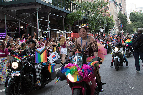 large red motorcycle festooned with pride colors with rider wearing tattoos and black lacy top