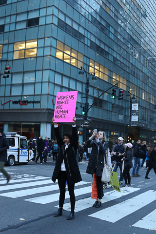 Woman stands in crosswalk holding sign up high womens rights are human rights