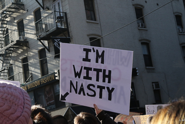 sign held high I'm with nasty build with fire escape in background