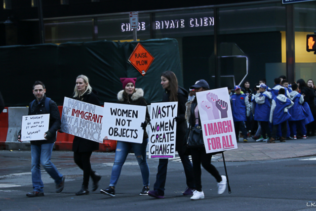 Four women and one man marching signs Nasty women create change, I march for all. women not objects. nation of immigrants not a notin of ignorance and I wouldn't be here if not for a woman