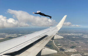 viewed out a plane window the wing and a woman dressed in black flying alongside