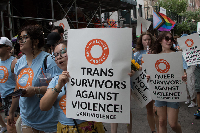 group in blue tee shirts with logo Anti Violence Project with signs Trans and Queer Survivors against Violence