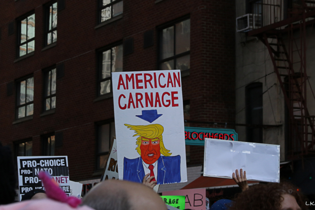 sign held above crowd with caricature of Trump and text American carnage