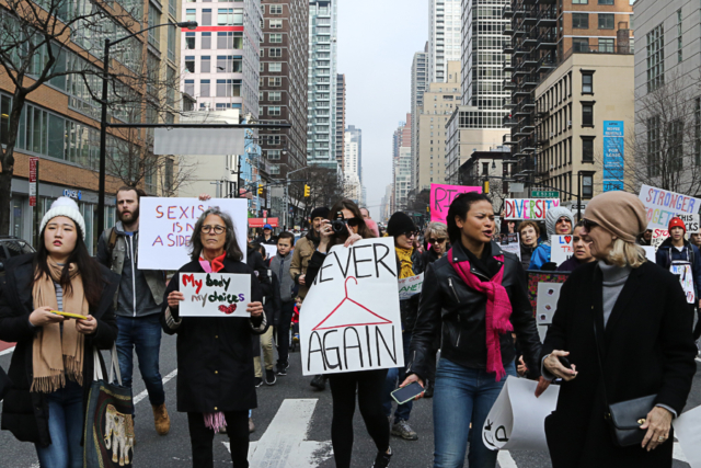 group shot of people at womens march one holds signs with drawing of hanger and says never again