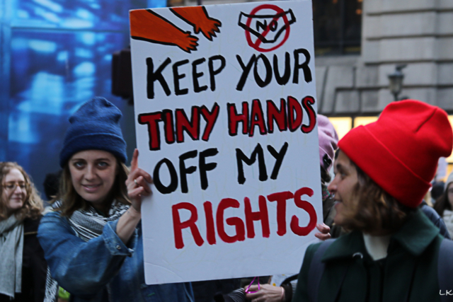 Two woman one looks to camera and holds sign Keep your tiny hands off my rights.