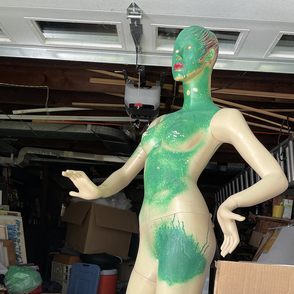 manniquin with green paint on front of body standing in garage