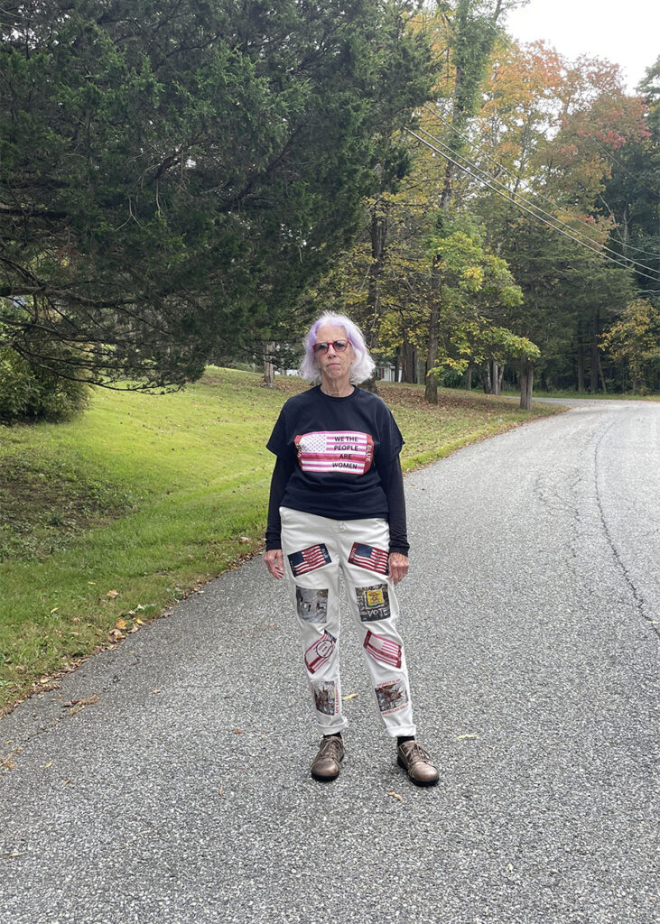 woman stands on road and is wearing black tee and white jeans with political vote blue messates