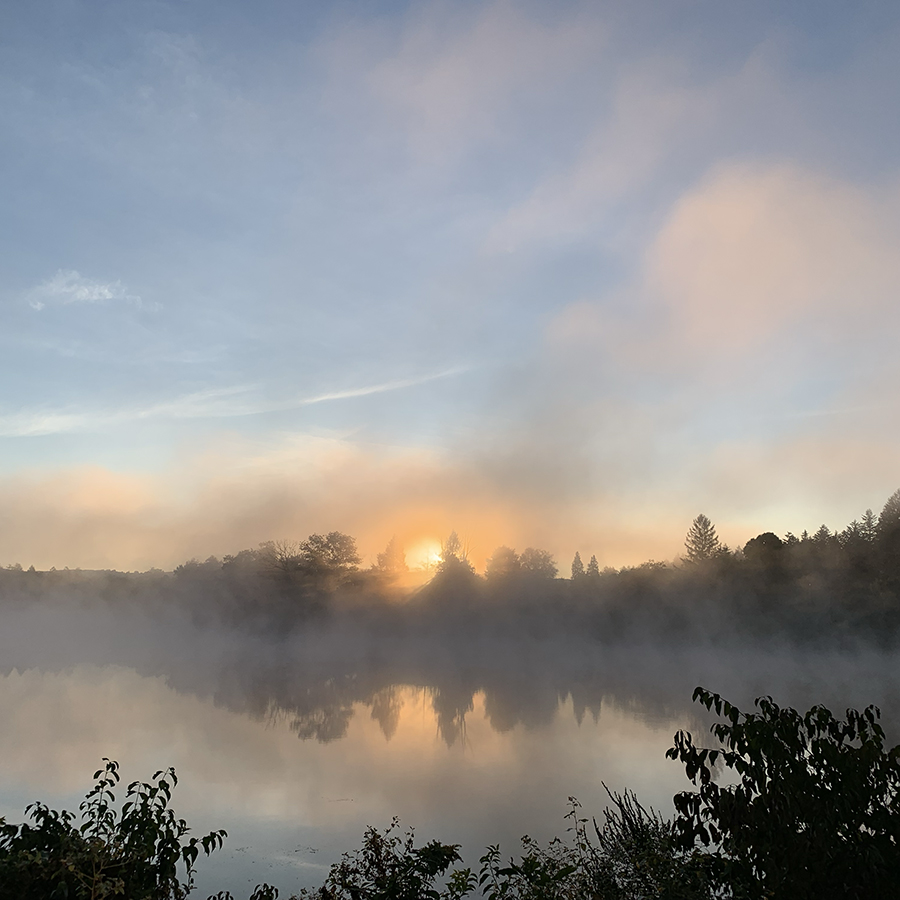 sun just breaking over hoirzon with golden light revlected in lake and blue sky