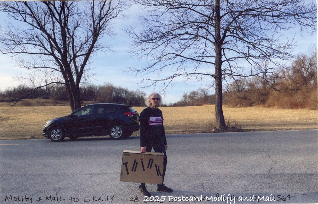 Woman dressed in black holdasa suitcase that reads Think, a road and fields are behind and a car drives by
