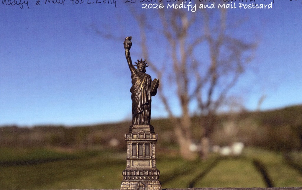 Statue of Liberty stands tall against farm fields, large tree and wintery hills in background